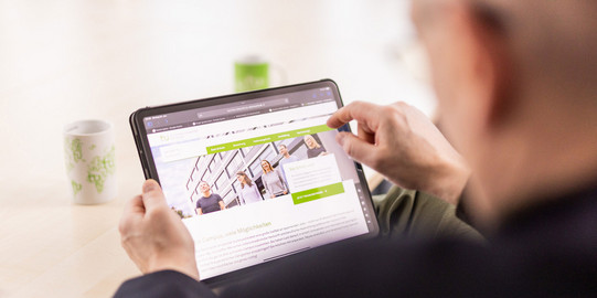 Mann mit Tablet in der Hand, der Bildschirm zeigt die Startseite der Karriere-Website der TU Dortmund an.