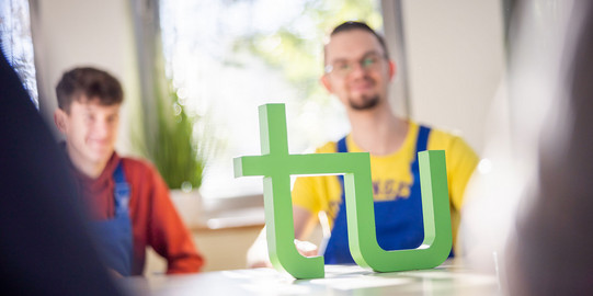 Auszubildende an einem Tisch, auf dem eine Figur des TU-Logos platziert ist.